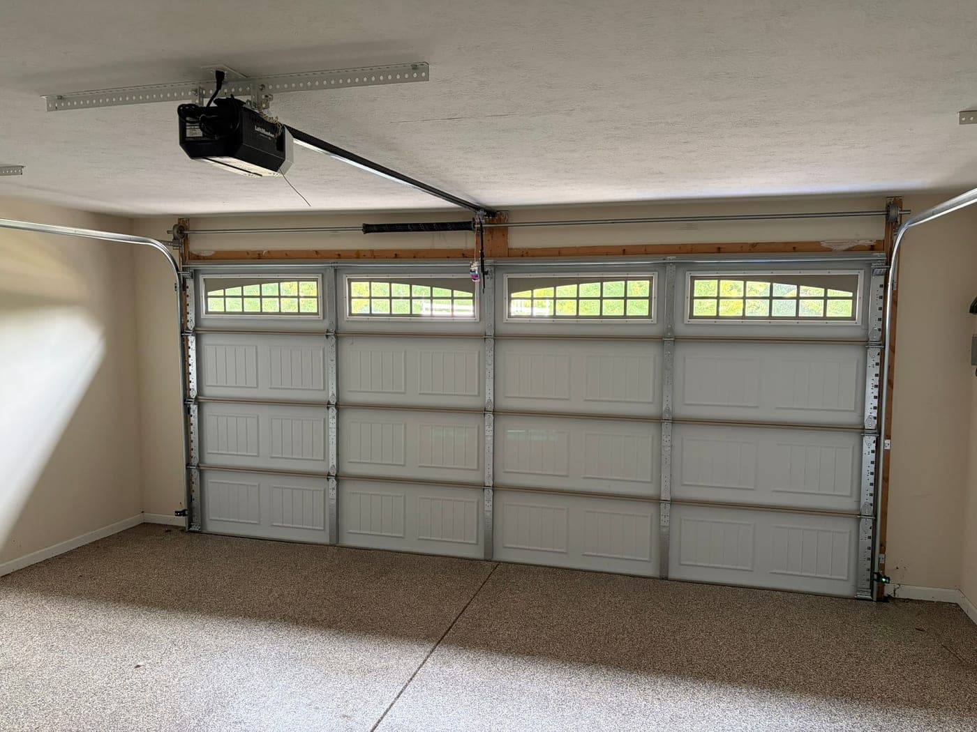 Inside a two-car garage: white sectional door with arched window row, torsion spring and a LiftMaster opener on the ceiling