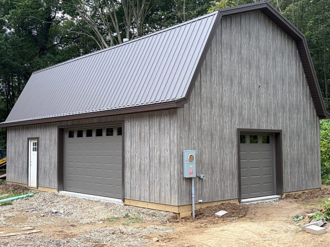 Two newly installed brown raised-panel garage doors with window rows on a gray pole barn